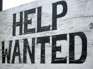 wooden board with slightly cracked white paint, "Help Wanted" in black print